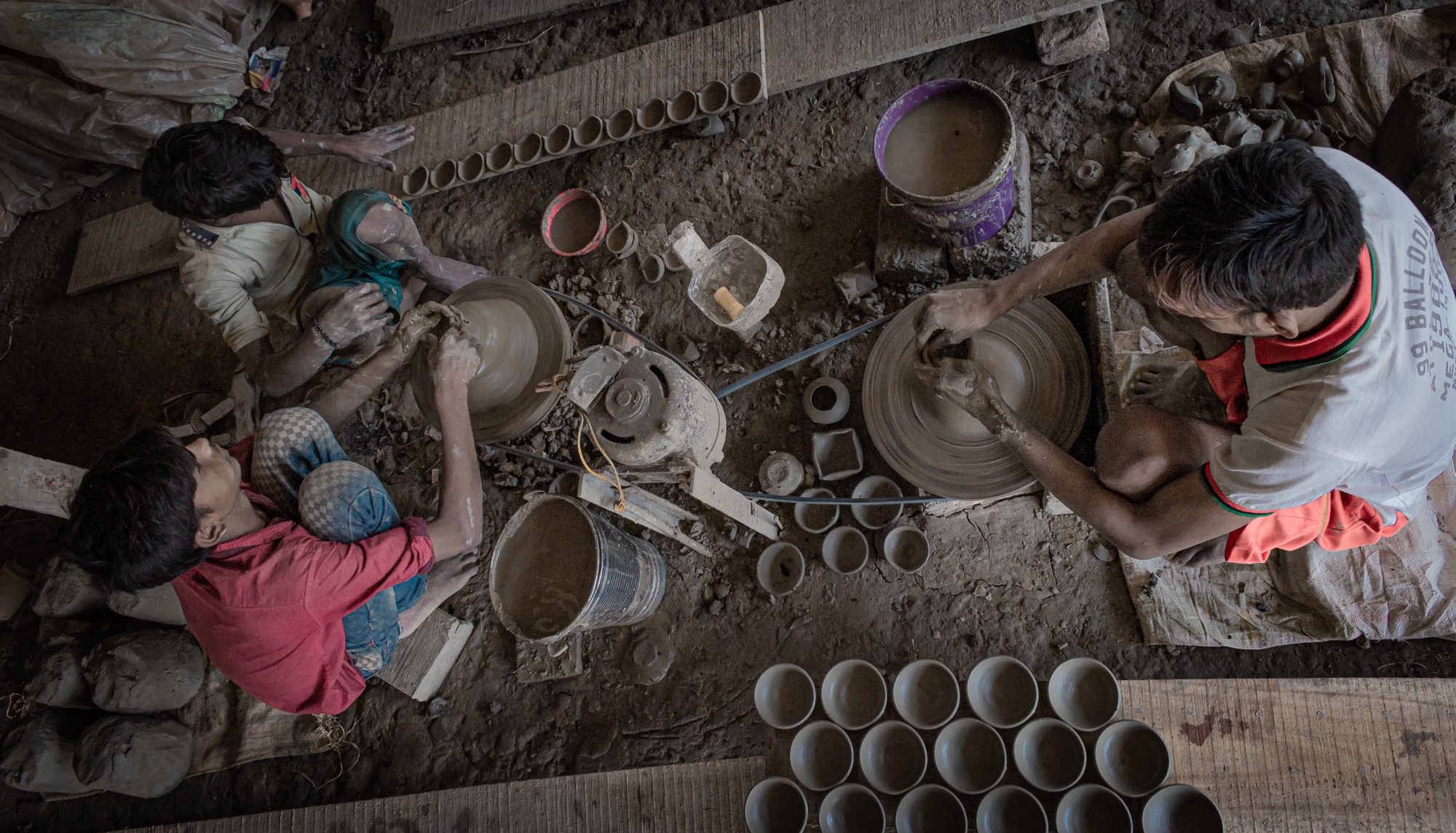Rows of freshly thrown bowls drying on a wooden plank